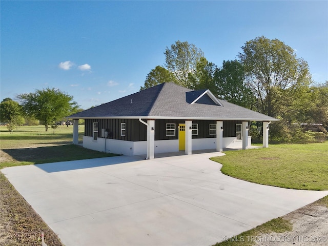 view of front of house featuring roof with shingles, concrete driveway, board and batten siding, a front yard, and a sunroom