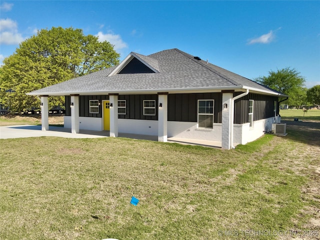 back of house featuring roof with shingles, central AC, board and batten siding, and a yard