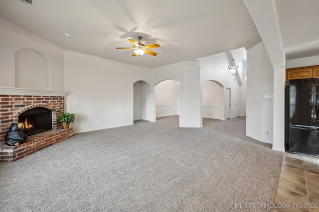 unfurnished living room featuring arched walkways, a fireplace, light colored carpet, visible vents, and ceiling fan