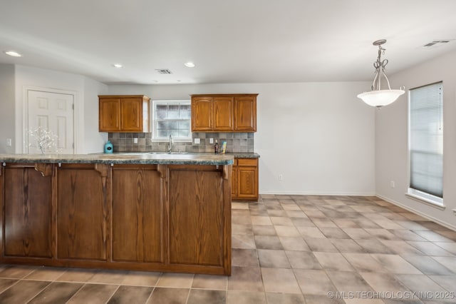 kitchen with tasteful backsplash, brown cabinetry, visible vents, and a kitchen breakfast bar