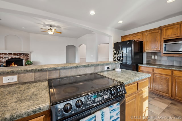 kitchen with black appliances, brown cabinetry, a brick fireplace, and backsplash