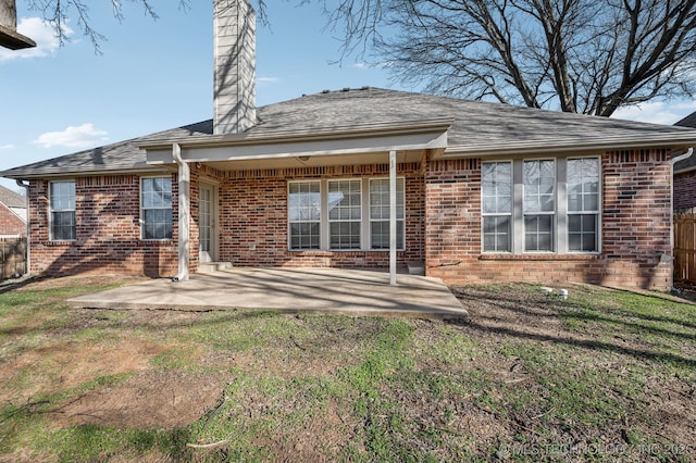 back of house with a patio area, brick siding, a lawn, and a chimney