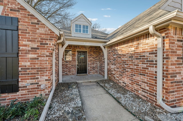 doorway to property featuring brick siding and roof with shingles