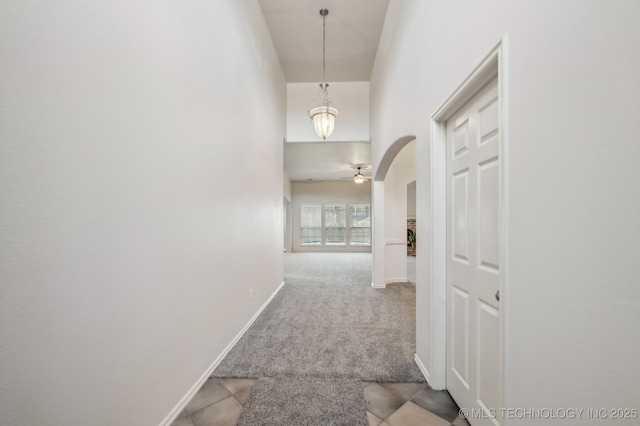 corridor with a towering ceiling, baseboards, arched walkways, and carpet flooring