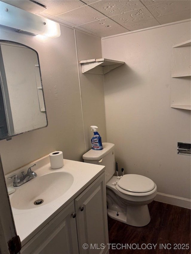 bathroom featuring a paneled ceiling, toilet, wood finished floors, vanity, and baseboards