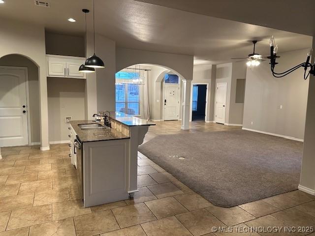 kitchen with arched walkways, light carpet, a sink, a ceiling fan, and dark countertops