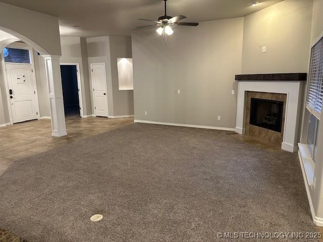 unfurnished living room with carpet, arched walkways, ornate columns, and a tile fireplace