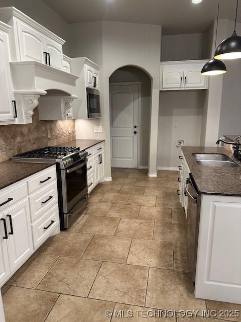 kitchen featuring decorative light fixtures, stainless steel appliances, backsplash, white cabinets, and a sink