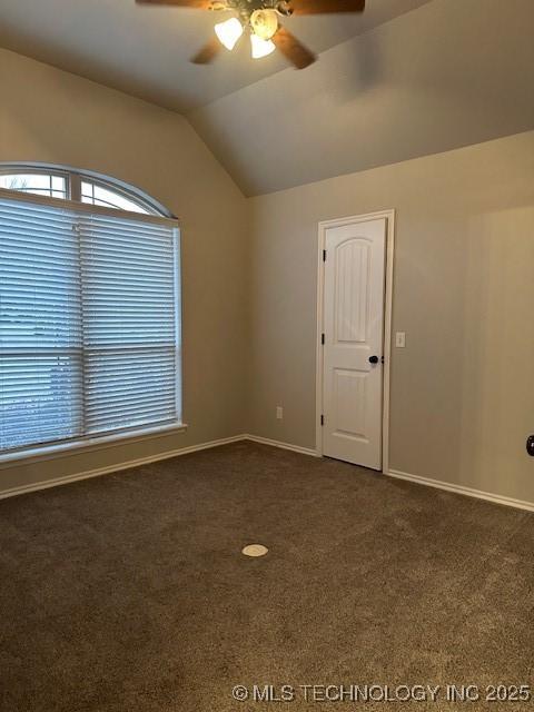 spare room with ceiling fan, dark carpet, vaulted ceiling, and baseboards