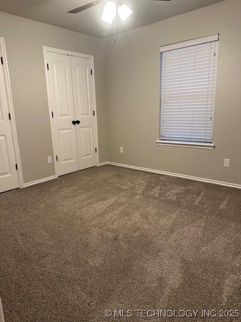 unfurnished bedroom with baseboards, dark carpet, ceiling fan, and a closet