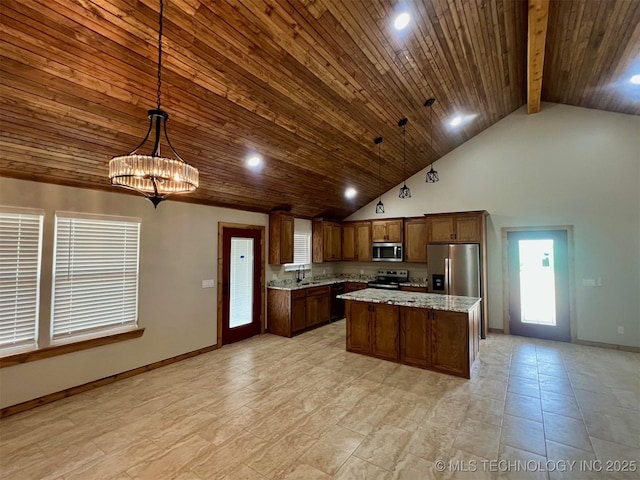 kitchen with baseboards, a kitchen island, appliances with stainless steel finishes, decorative light fixtures, and a sink