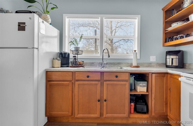 kitchen featuring brown cabinets, open shelves, light countertops, freestanding refrigerator, and a sink