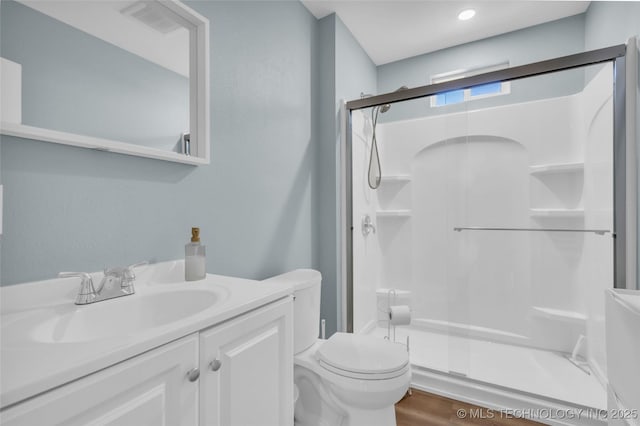 bathroom featuring wood finished floors, a stall shower, vanity, and toilet