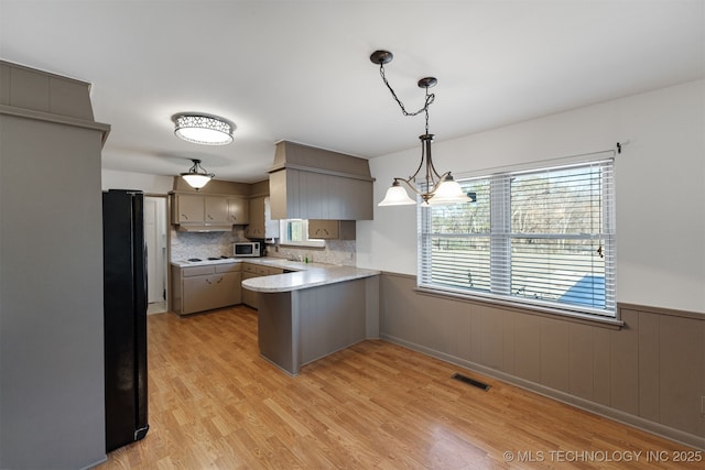 kitchen with light wood finished floors, visible vents, a wainscoted wall, freestanding refrigerator, and a peninsula