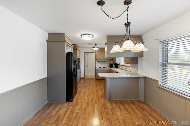 kitchen with light wood-style flooring, backsplash, wainscoting, a peninsula, and black fridge