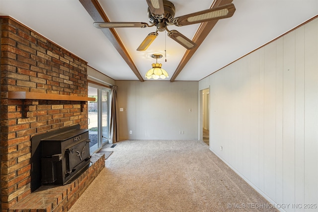 unfurnished living room with a ceiling fan, a wood stove, light carpet, and beamed ceiling