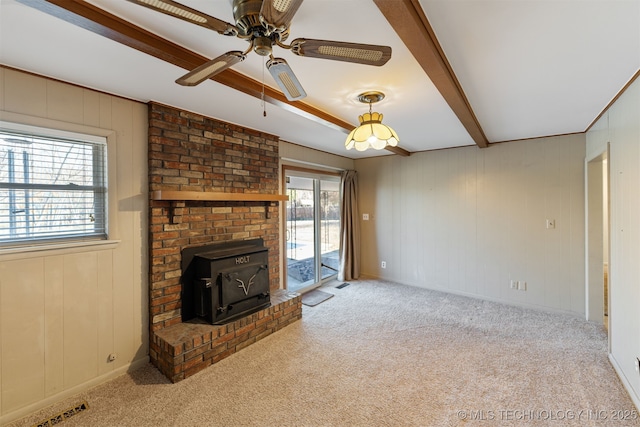 unfurnished living room featuring a wood stove, carpet, visible vents, and beam ceiling