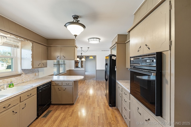 kitchen with a peninsula, a sink, light countertops, light wood-type flooring, and black appliances