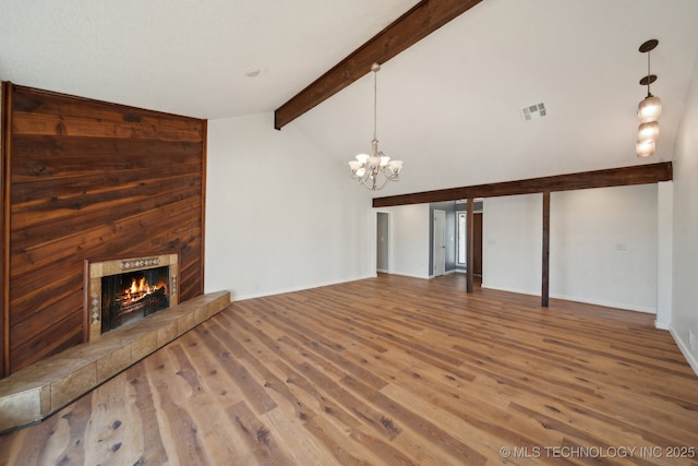 unfurnished living room featuring baseboards, visible vents, a tile fireplace, wood finished floors, and beam ceiling