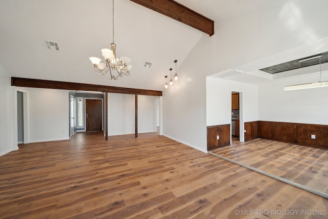 spare room with a wainscoted wall, a notable chandelier, visible vents, wood finished floors, and beamed ceiling