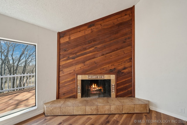 interior details featuring a textured ceiling, a tiled fireplace, wood finished floors, and baseboards