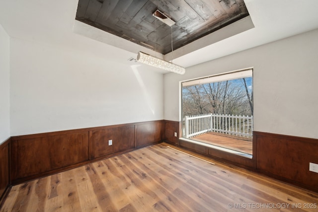 spare room featuring a raised ceiling, wainscoting, wooden walls, and wood finished floors