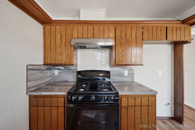 kitchen with wood finished floors, range hood, brown cabinets, tasteful backsplash, and black gas range oven