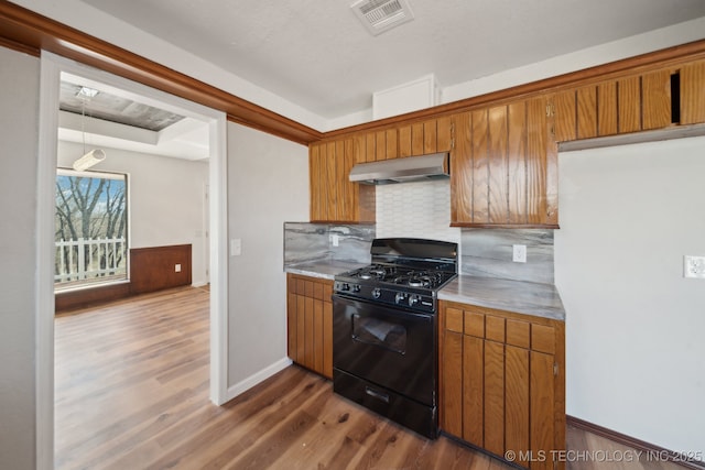 kitchen featuring under cabinet range hood, visible vents, black range with gas stovetop, brown cabinets, and dark wood-style floors