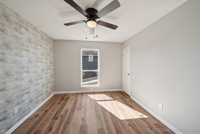 spare room with a textured ceiling, wood finished floors, visible vents, and baseboards