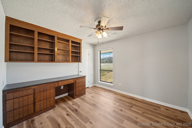 unfurnished office with ceiling fan, built in study area, light wood-style flooring, and baseboards