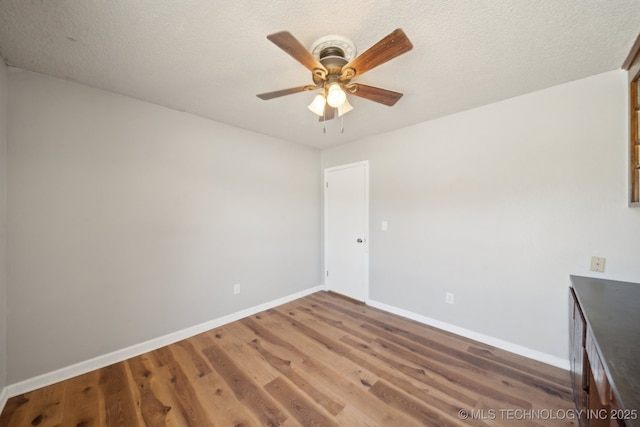 empty room with ceiling fan, a textured ceiling, baseboards, and wood finished floors