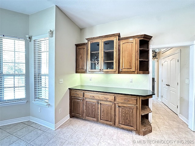 kitchen featuring dark countertops, baseboards, glass insert cabinets, and open shelves