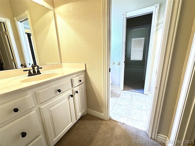 bathroom featuring baseboards, a textured wall, toilet, tile patterned flooring, and vanity