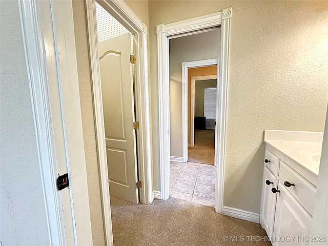 corridor featuring light carpet, a textured wall, and baseboards