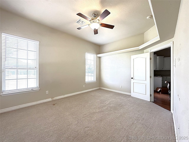 carpeted spare room featuring a textured ceiling, baseboards, visible vents, and a ceiling fan