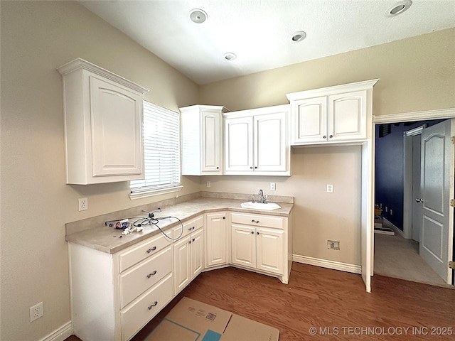 kitchen featuring light countertops, dark wood-type flooring, a sink, and white cabinets