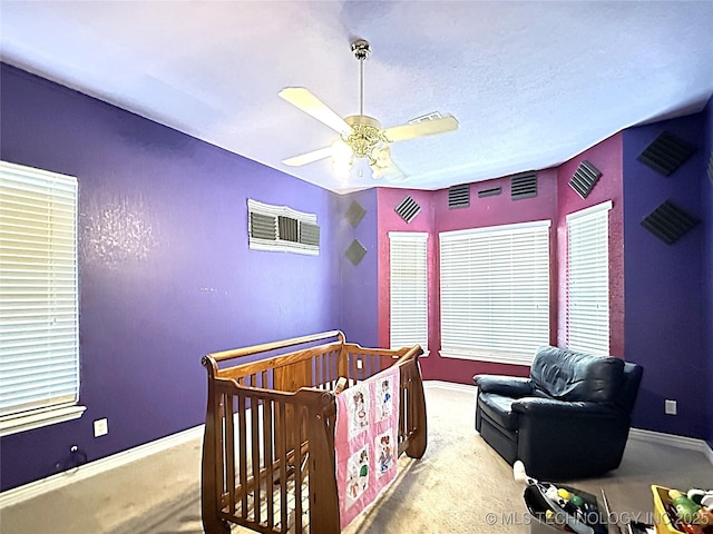 carpeted bedroom featuring a nursery area, ceiling fan, and baseboards