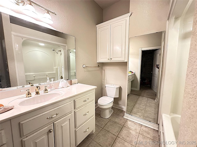 bathroom featuring tile patterned floors, a textured wall, toilet, vanity, and walk in shower