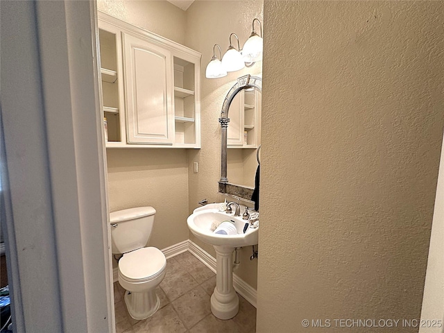 bathroom with toilet, a textured wall, baseboards, and tile patterned floors