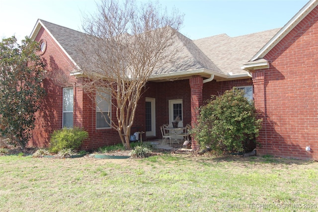 single story home featuring a patio area, a front lawn, a shingled roof, and brick siding