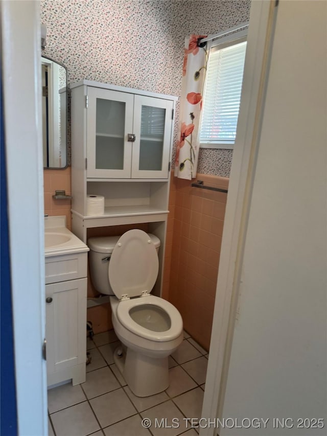 bathroom with toilet, a wainscoted wall, tile patterned flooring, vanity, and tile walls