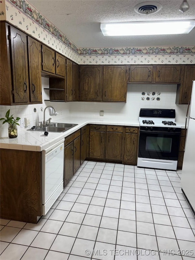 kitchen featuring visible vents, a sink, a textured ceiling, dark brown cabinetry, and white appliances