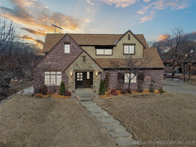 view of front facade featuring stone siding, roof with shingles, and brick siding