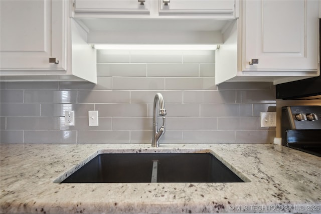 kitchen featuring a sink, decorative backsplash, light stone countertops, and white cabinets