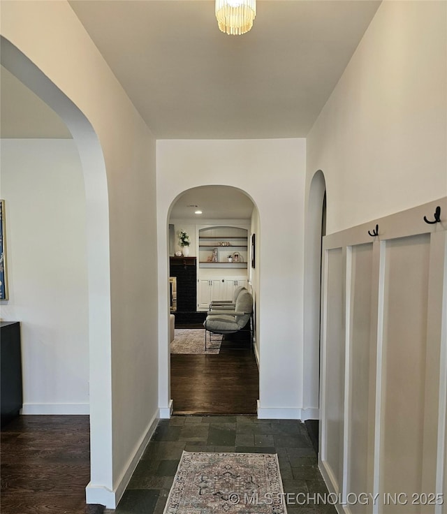 hall with stone tile flooring, built in shelves, baseboards, and arched walkways