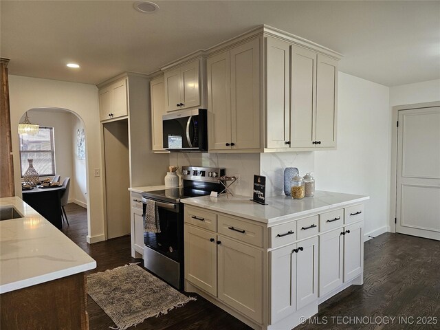 kitchen featuring light stone counters, dark wood finished floors, arched walkways, appliances with stainless steel finishes, and backsplash