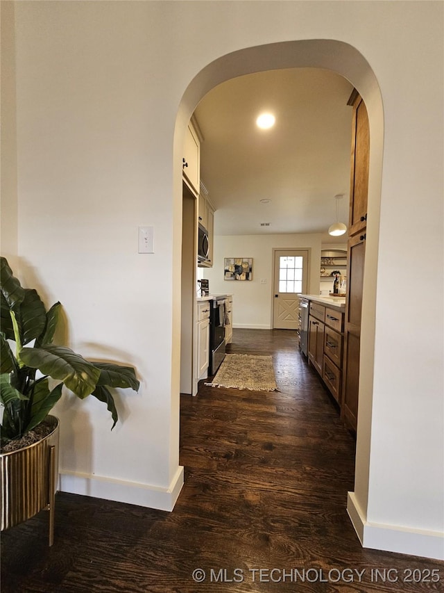 hallway featuring baseboards, arched walkways, and dark wood-style flooring