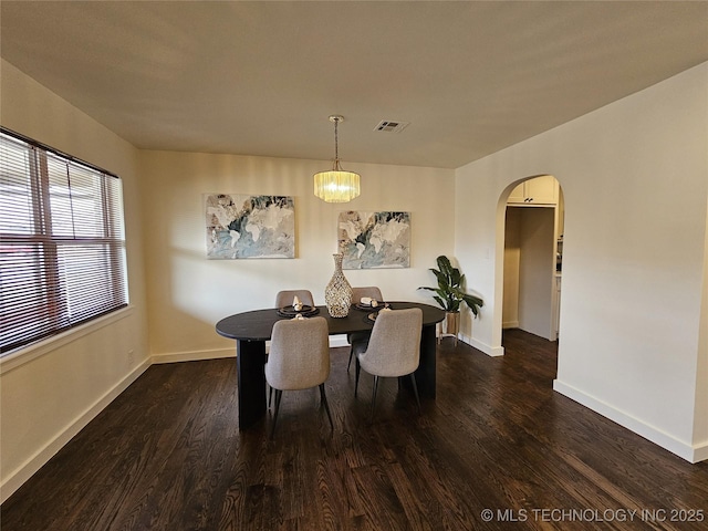 dining room featuring dark wood-style floors, arched walkways, and baseboards