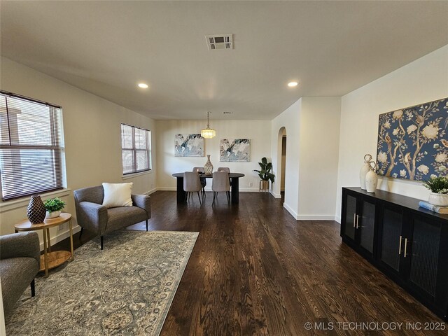 living area featuring dark wood-style floors, arched walkways, visible vents, and baseboards