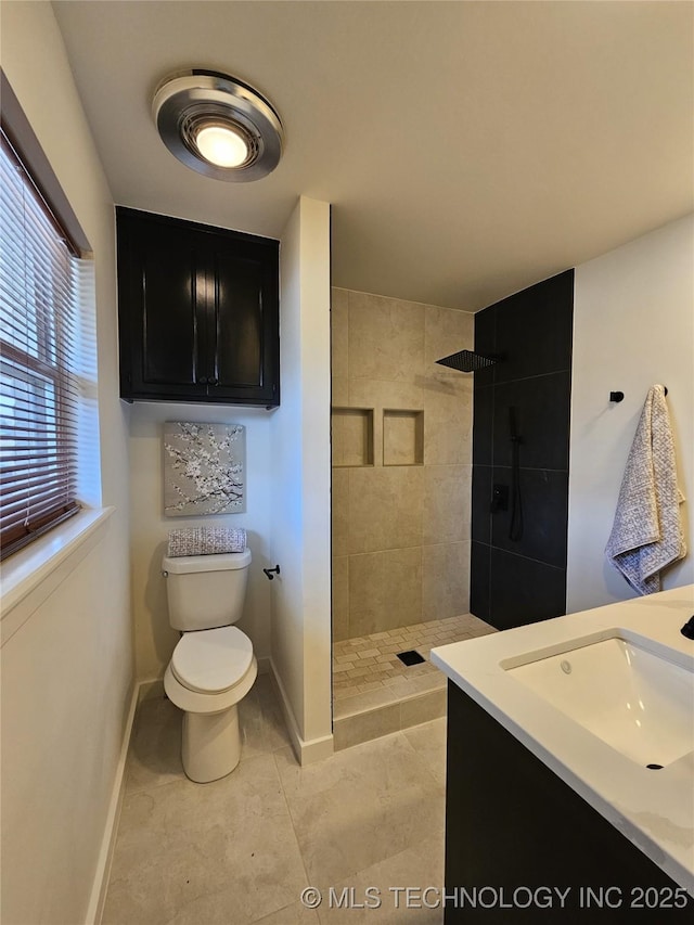 bathroom featuring a tile shower, toilet, baseboards, and a sink